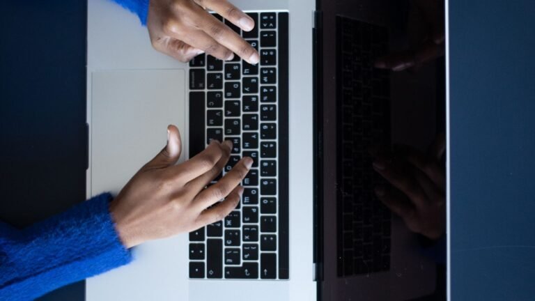Hands typing on a laptop keyboard in low light