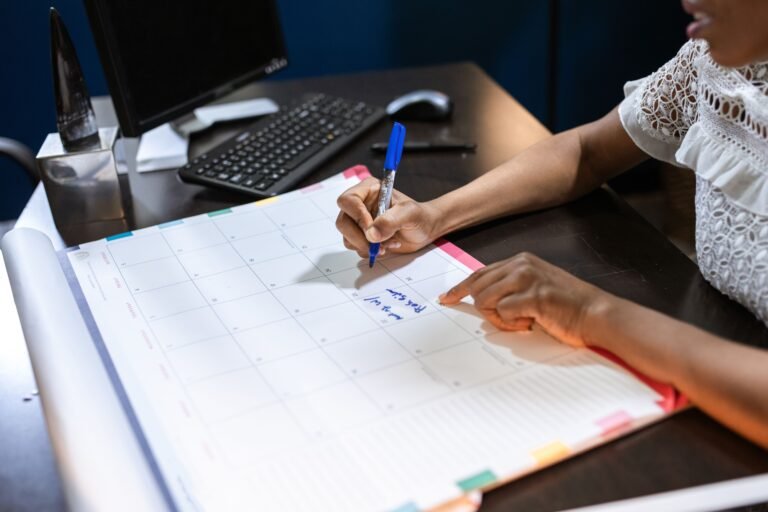 A person writing on a desk calendar with a pen while planning their schedule
